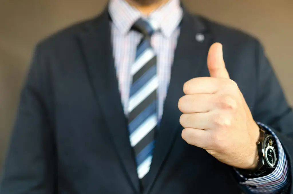 Close-up of a businessman in a suit giving a thumbs up gesture, symbolizing success.